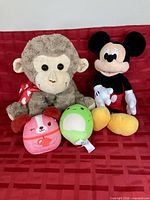 Monkey plush, Mickey Mouse plush, two Squishmallows on red background