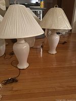 Two glossy white ceramic table lamps with pleated shades