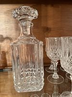 Square cut crystal decanter with stopper, surrounding crystal stemware visible