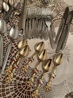 Array of assorted cutlery including forks, knives, stainless spoons and four gold-tone enamel souvenir spoons