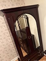 Full view of cherry wood armoire showing mirrored doors and crown molding