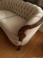 Side angle showing carved wood arm and beige upholstery