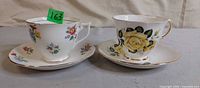 Both teacup and saucer sets side by side showing patterns and gold trim