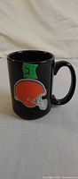 Front view of black ceramic mug showing raised orange football helmet graphic