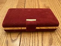 Closed red velvet jewelry case with gold-tone trim on wooden surface