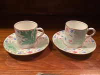 Two demitasse cups each on a saucer showing pattern and gold trim