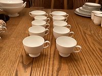 Eight white Wedgwood cups arranged on wooden table