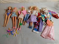 Five Barbie dolls laid out with extra clothing pieces and accessories