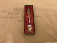 Full view of boxed souvenir spoon showing crest, spoon bowl, packaging text
