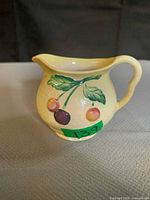 Front view of yellow Carlton Ware creamer showing fruit motif and handle