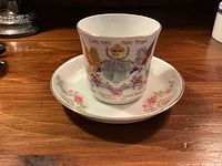 Cup front view showing royal portraits, crest and coronation text