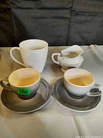 Group photo showing two grey Le Creuset espresso cups on matching saucers, a white textured mug, and a small floral creamer