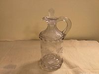 Full view of clear pressed glass cruet with stopper showing pattern and handle