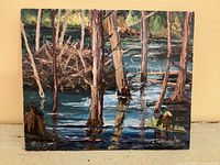 Front view of signed oil painting depicting beaver lodge in wooded wetland, signature visible