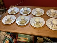 Eight complete place settings of Minton Laurentian china displayed on table, each stack shows cup, saucer, and three graduated plates