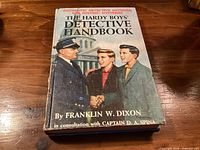 Front cover of The Hardy Boys' Detective Handbook hardcover with dust jacket on wooden table