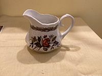 Front view of white ceramic creamer with rose design and brown band