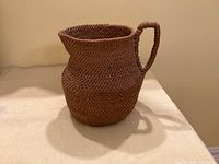 Front view of brown woven wicker basket shaped like a pitcher with handle
