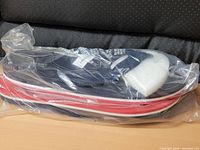 Pair of flip flops sealed in plastic bag, side view shows red-white striped midsole