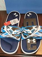 Top view of sandals showing patterned strap, navy footbed, attached size tag