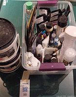 Plastic bin containing various acrylic paint bottles, tubes, metal leaf packs and accessories, plus two Liquitex gesso buckets