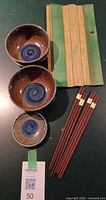 Overall lot showing two ceramic bowls, one sauce dish, two pairs chopsticks, and green bamboo sushi mat