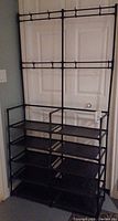 Full view of black tubular plastic storage unit with five shelves and top hooks