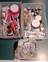 Overview of three plastic bins containing various opened acrylic paint tubes, jars and bottles