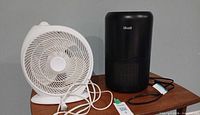 Black Levoit Core 300 air purifier beside white tabletop fan on table