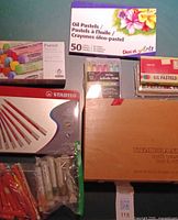 Overview showing Pentel oil pastels box, Stabilo pastel pencil tin, Rembrandt wooden pastel box, assorted paint sticks and crayons