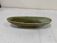 Side view of oval green glazed dish showing fluted sides and overall shape
