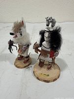 Front view of both wooden folk art dolls showing painted details, fur, leather and bases