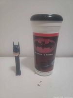 Batman PEZ dispenser beside Batman & Robin logo tumbler front view