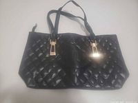Front view of black quilted faux leather tote showing handles and gold-tone hardware
