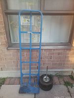 Full view of blue steel hand truck frame standing upright next to window