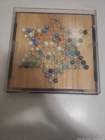 wooden Chinese checkers board filled with assorted glass marbles inside clear plastic case