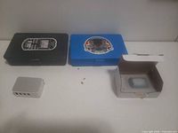 All items closed: black and blue storage boxes, USB charger, battery in open carton, loose screws