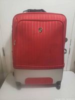Front view of suitcase showing red fabric front panel, silver base, wheels