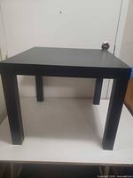 Full view of black laminate square table on platform