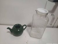 green ceramic teapot and clear ribbed glass pitcher side by side