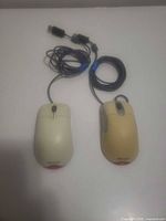Top view of two wired USB mice showing beige and yellow shells, scroll wheels and cables