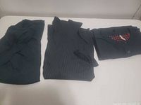Three folded garments laid out: trousers, ribbed sweater, button cardigan