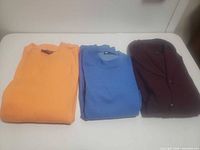 Three folded sweaters: orange, blue, burgundy on tabletop
