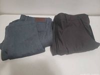 Two folded pairs of men's dress pants, blue textured and dark brown, on table