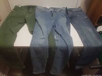 Three pairs of pants laid out: green, light blue distressed, dark blue