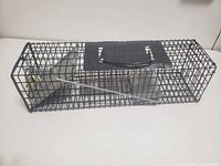 Side view of metal wire mesh live-catch mouse trap showing bait plate, trigger rod, and top handle