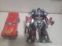 Overall view of Optimus Prime figure beside red flame toy car