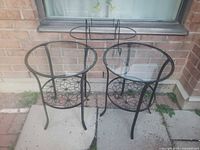 Pair of round black metal tables with glass tops positioned outdoors