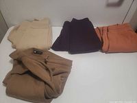 Four pairs of sweatpants in beige, camel, purple and rust laid out on table