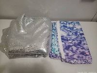 Silver sequin fabric folded and stacked next to folded printed polyester fabric